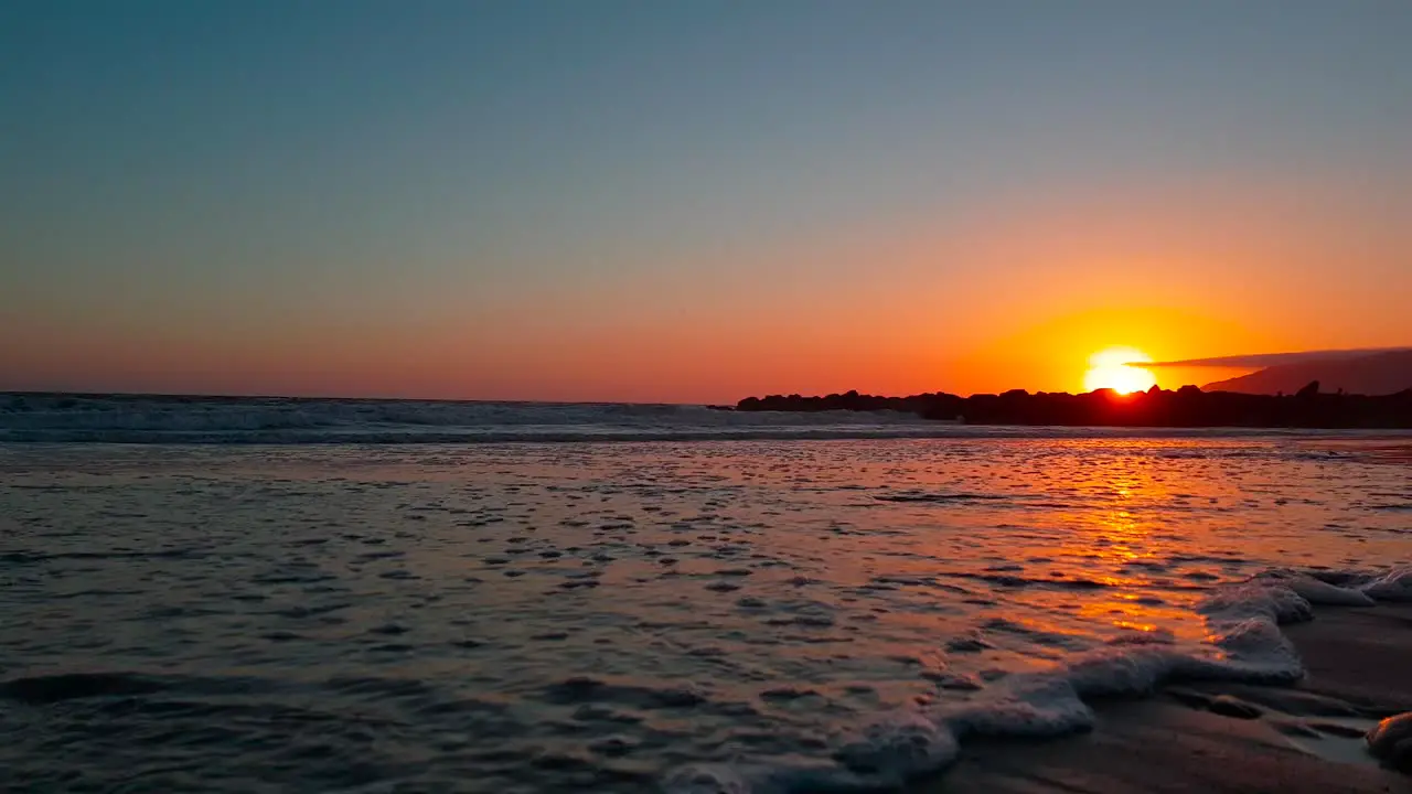 Very low gimbal shot of beach at sunset following waves crashing at San Buenaventura State Beach in Ventura California United States