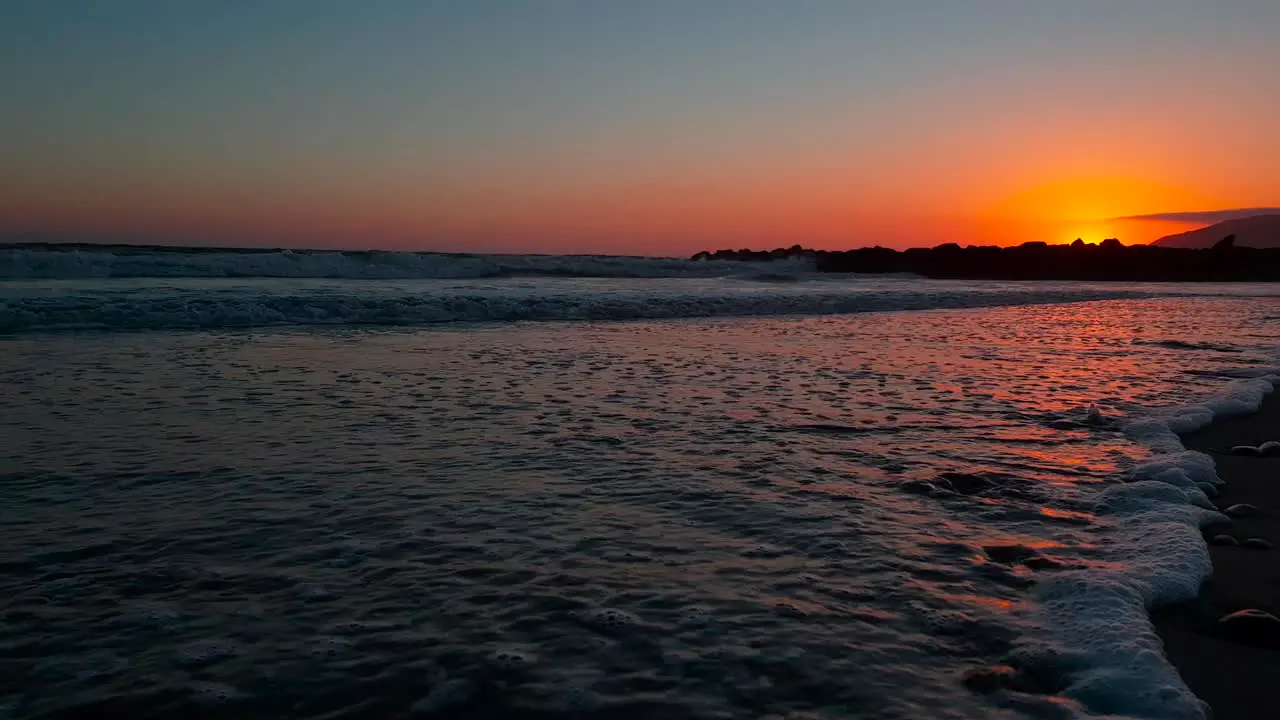 Low dolly shot of beach during sunset with sunlight reflecting beautifully on the sand and waves coming in at San Buenaventura State Beach in Ventura California USA