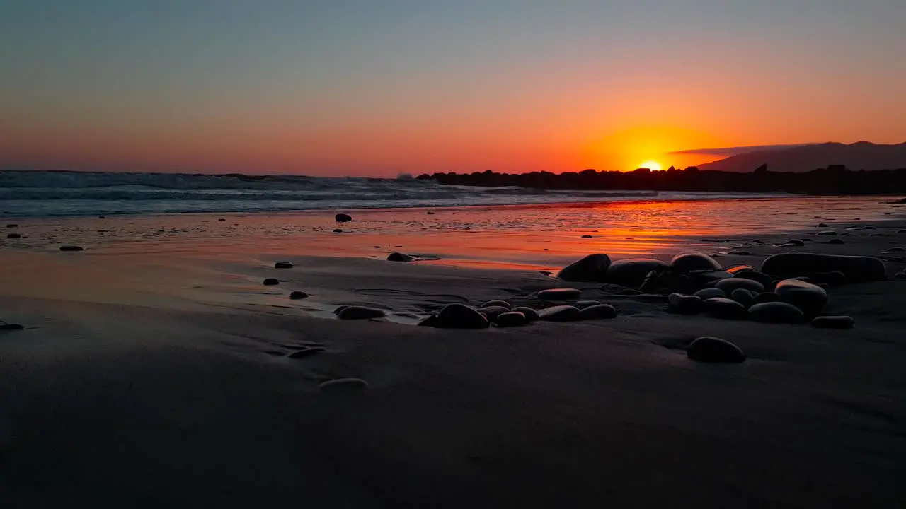 Low dolly shot of pebbles at beach during sunset with sunlight reflecting beautifully on the sand at San Buenaventura State Beach in Ventura California USA