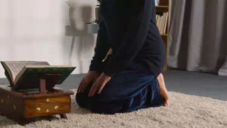 Close Up Of Muslim Woman At Home Kneeling And Reciting From The Quran