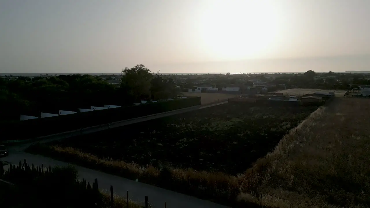 Country shot from a drone starting close to a dry grassy field and rising up looking towards the sunset above the Atlantic sea