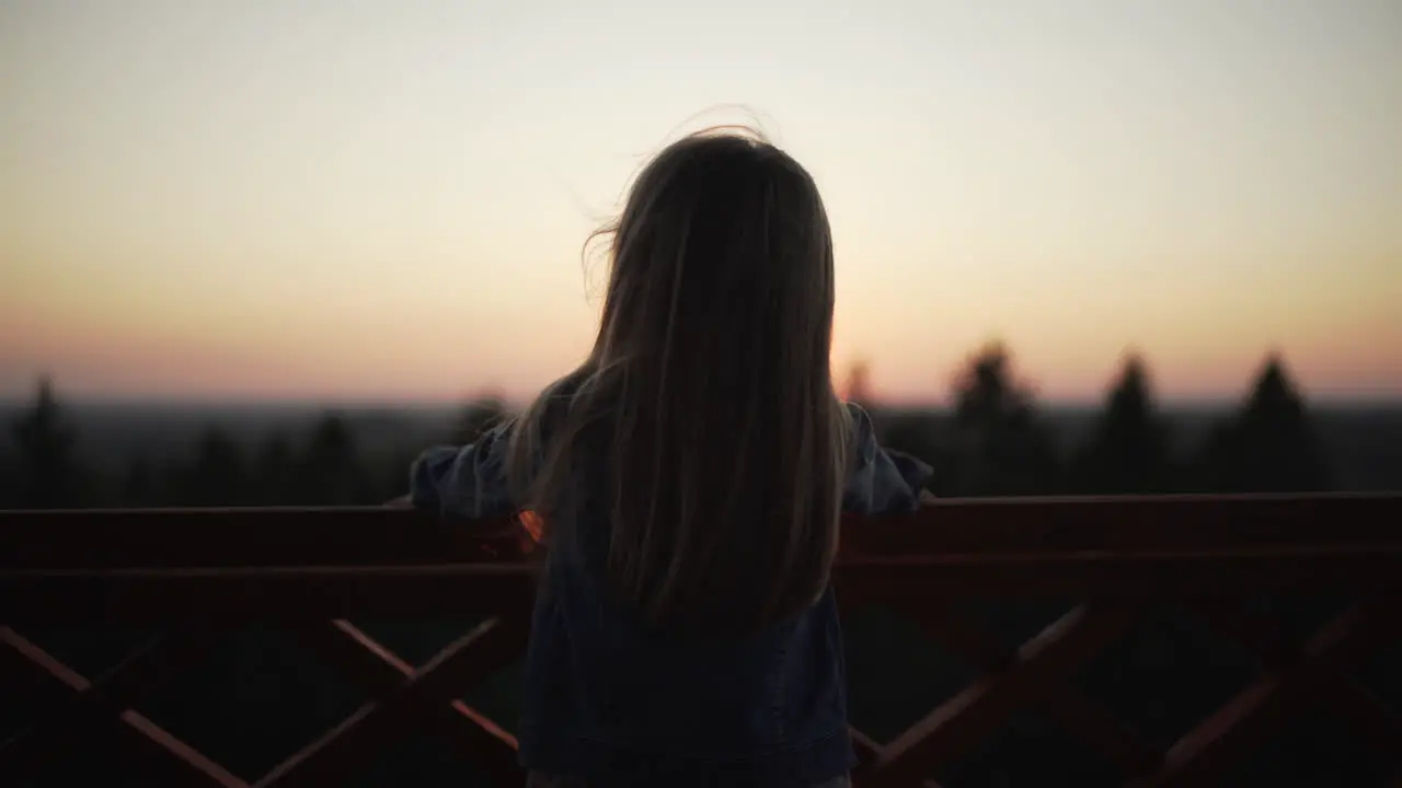 Silhouette of little girl standing on watchtower at sunset