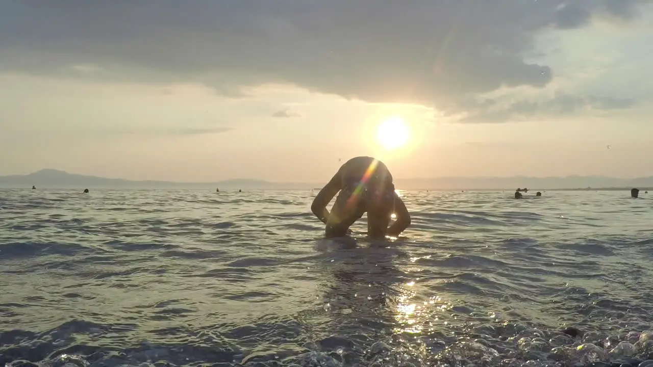 Kid plays at the waves with sunset on the background at Kalamata beach Greece