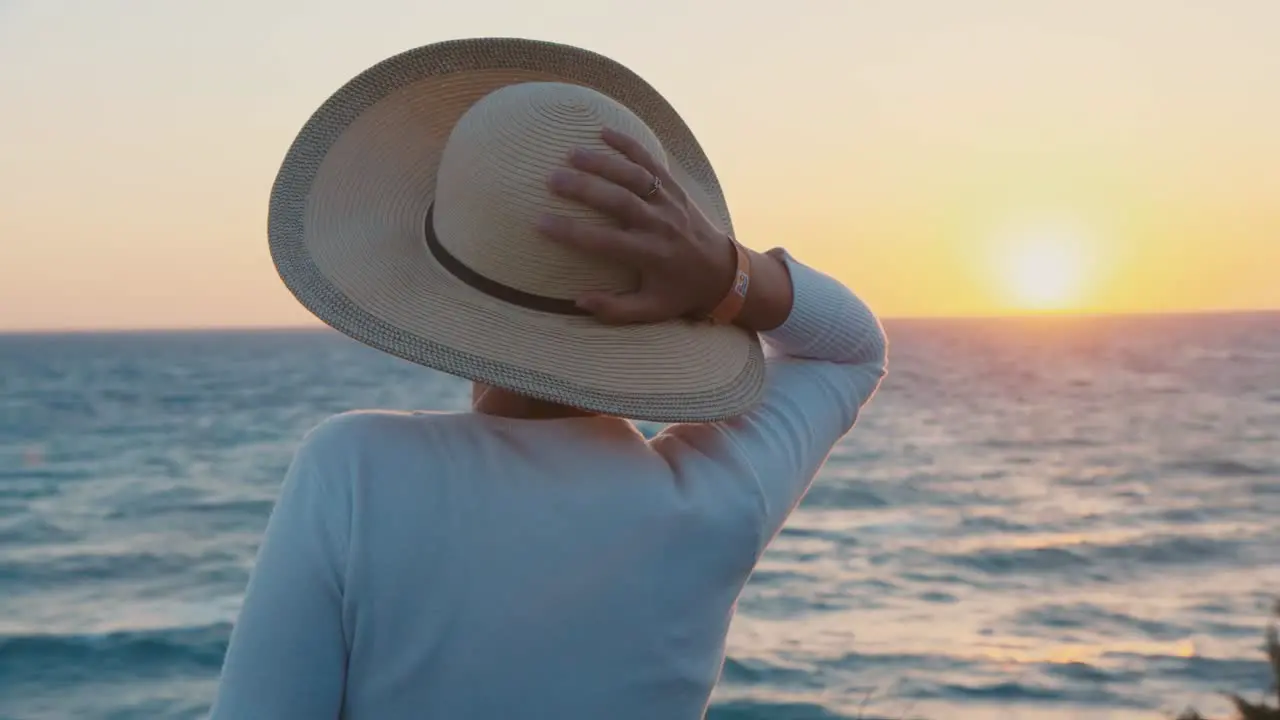 A woman in a hat looks at the sunset over the sea