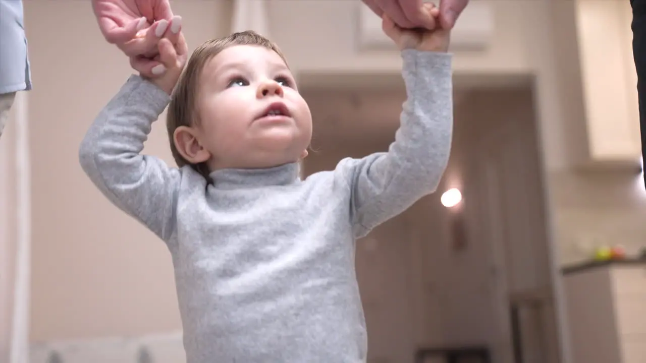 Parents Holding Their Baby's Hands Helping Him Take His First Steps At Home 2