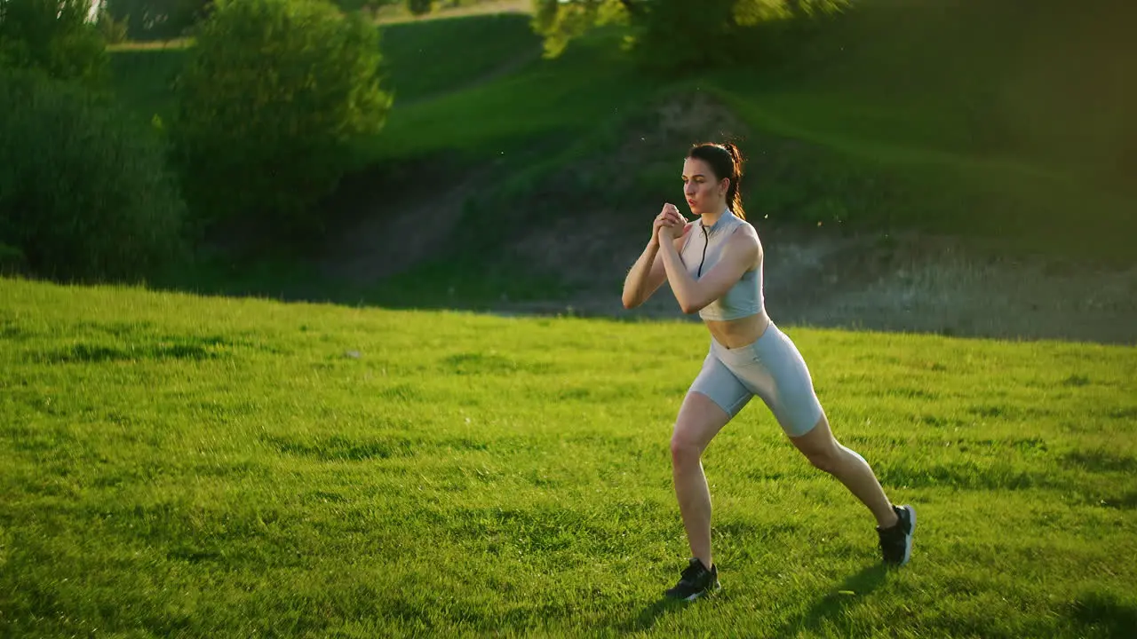 A woman makes lunges during a training session in the park and raises her leg in the knee