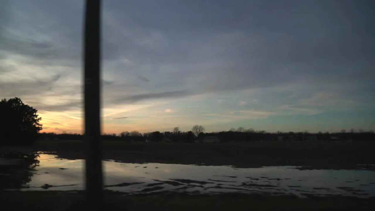 Car Side Window View While Driving Past Farm Country During Peaceful Sunset