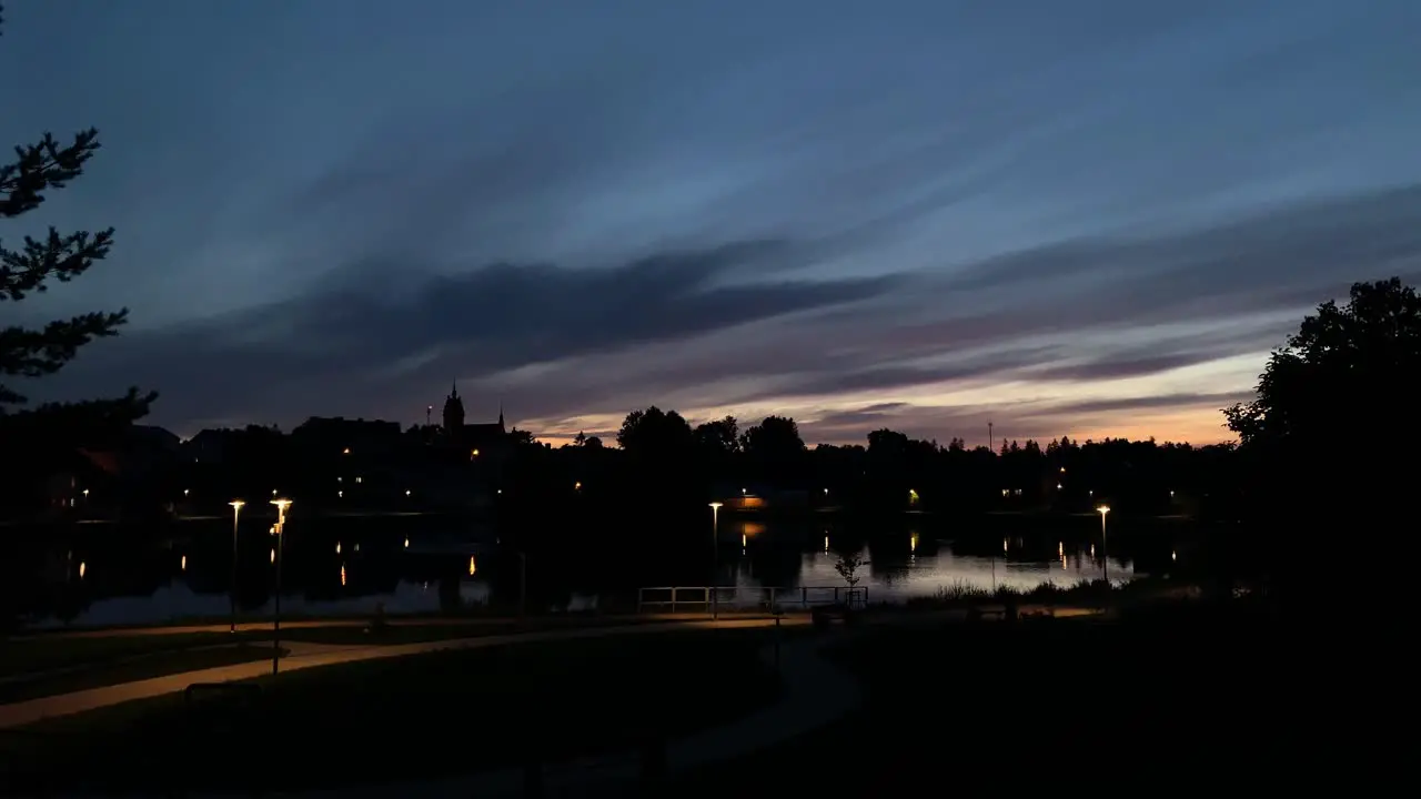 Darkening timelapse of blue hour sunset over urban park lake reflection with path