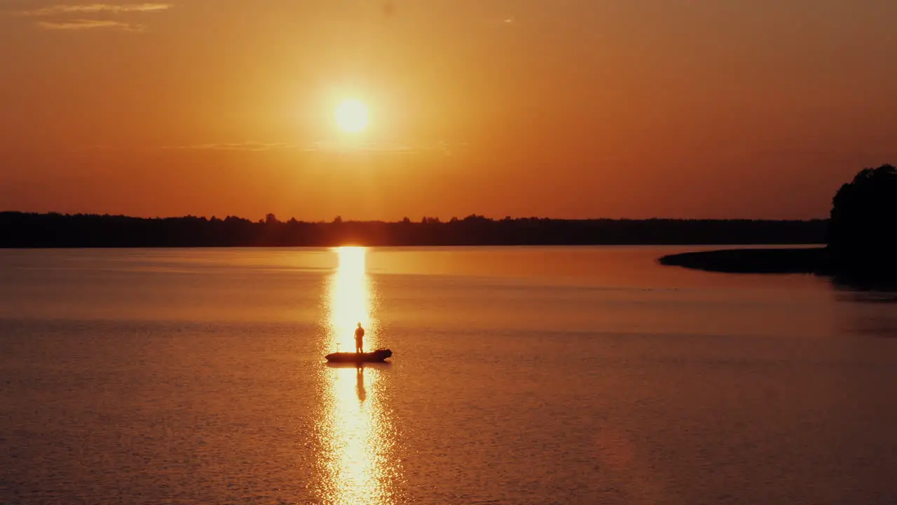 Aerial shot of men fishing from the boat in front of shiny sun at evening