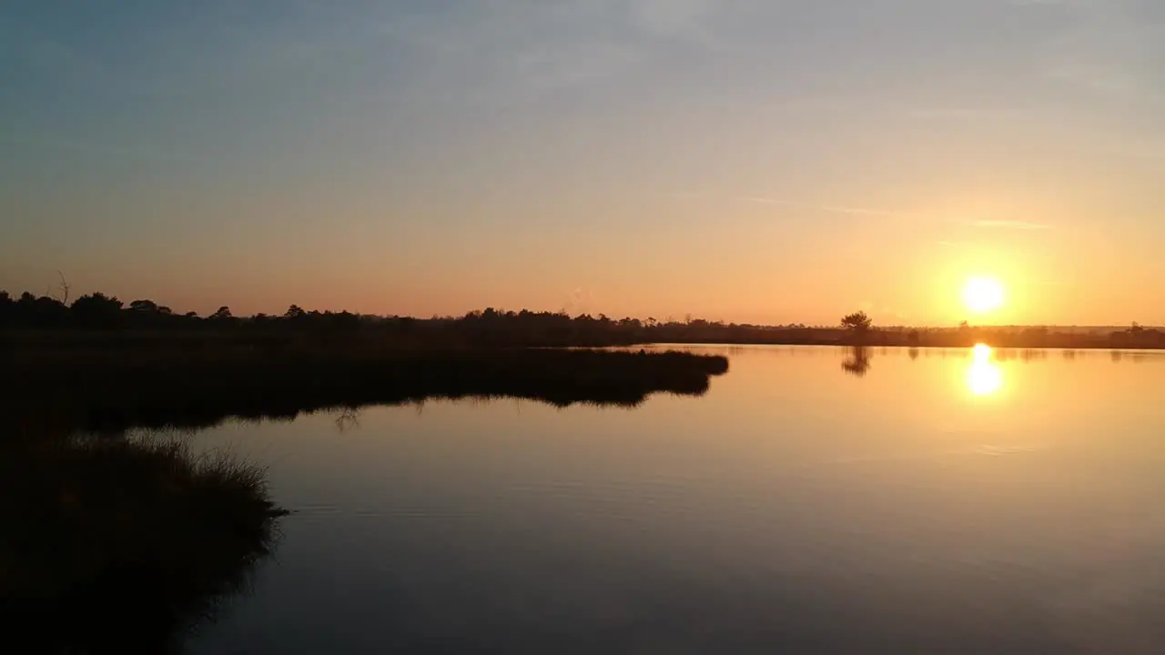 Aerial push out over water beautiful sunset lake silhouette teal orange sky