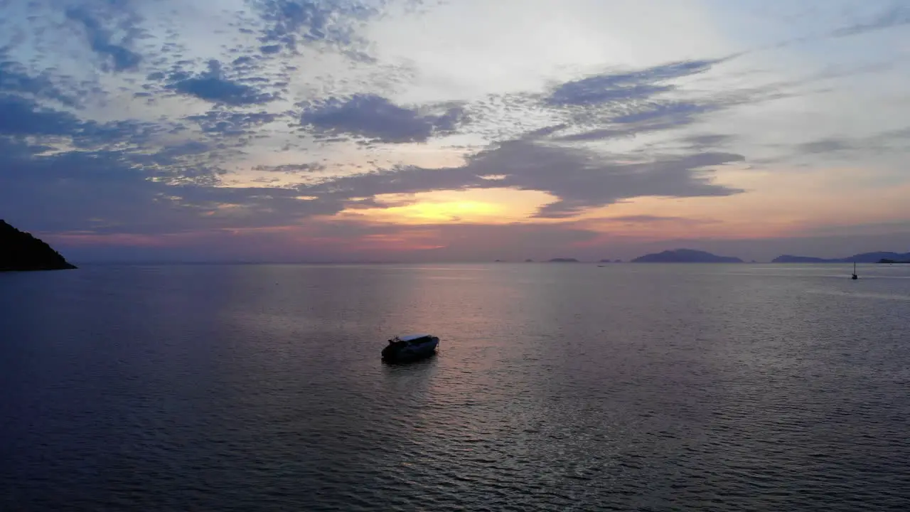 Drone footage of boats anchored on a peacefull ocean with a coloful sunset on the background