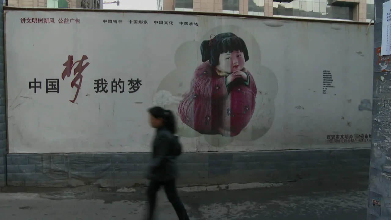 Chinese factory workers walk home through an alleyway and past a large billboard