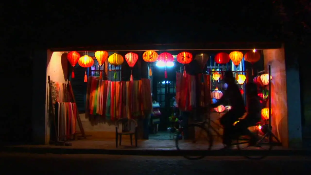 Bicycles and rickshaws pass a colorful lantern store at night in Vietnam