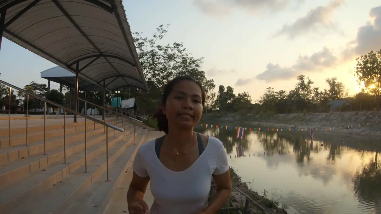 A slowmotion close up shot of a girl jogging in the centre of the frame towards the camera she is jogging in the park near a small lake during sunset