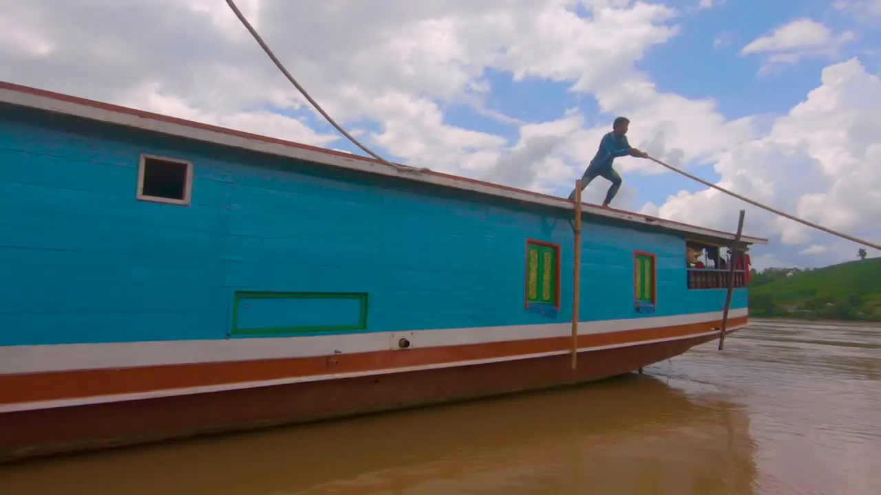 A local sailor pushes a boat away from the shore launching it down the Mekong river with tourists on