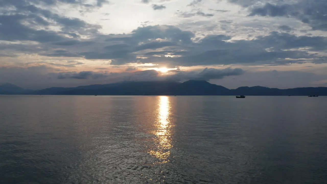 Beautiful Vietnamese landscape of a golden sunset reflecting over the ocean with mountains and traditional fishing boat