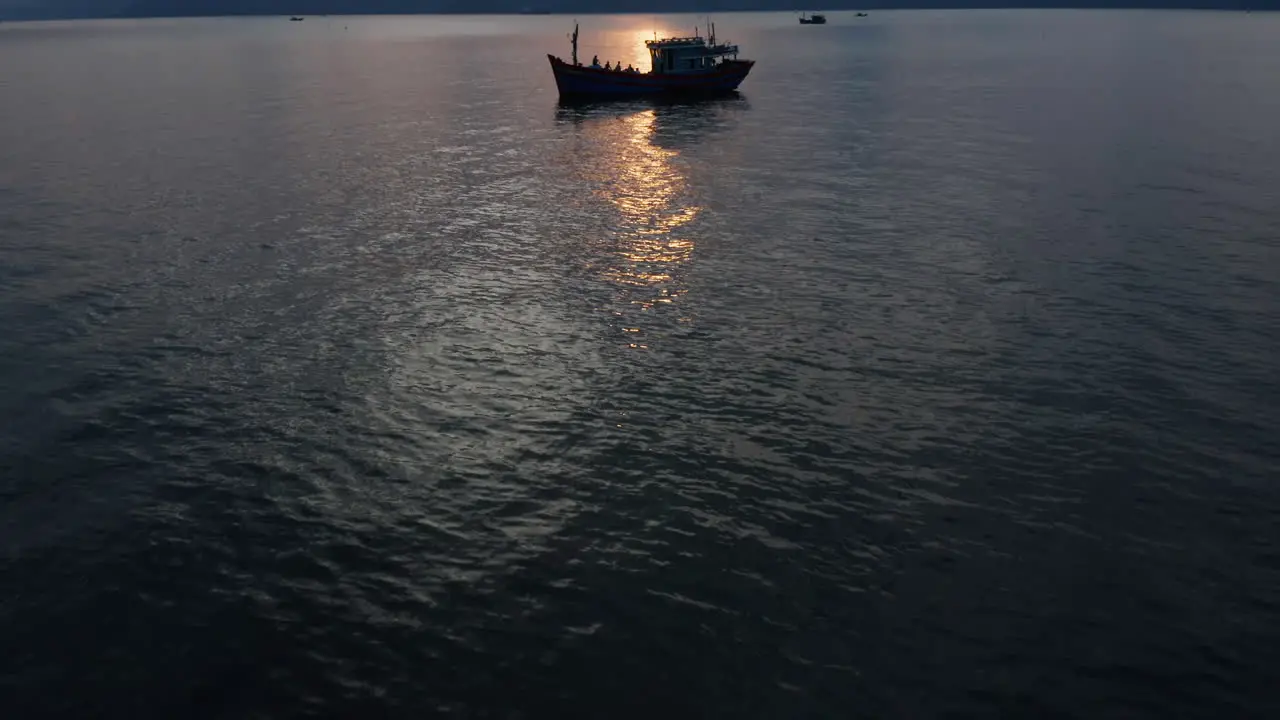 Reveal shot of a beautiful Vietnamese landscape of ocean mountains and a silhouette of a traditional fishing boat docked at sunset