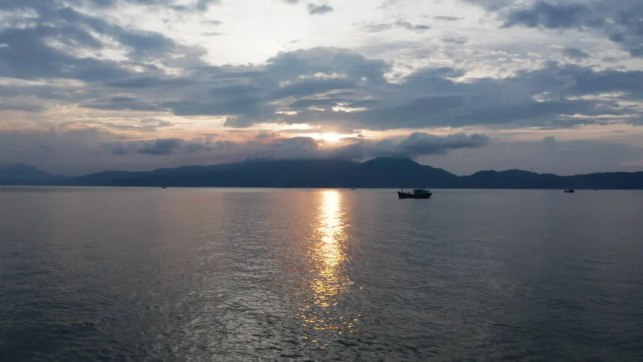 Beautiful Vietnamese landscape of golden sunset reflecting over ocean with mountains and traditional fishing boat