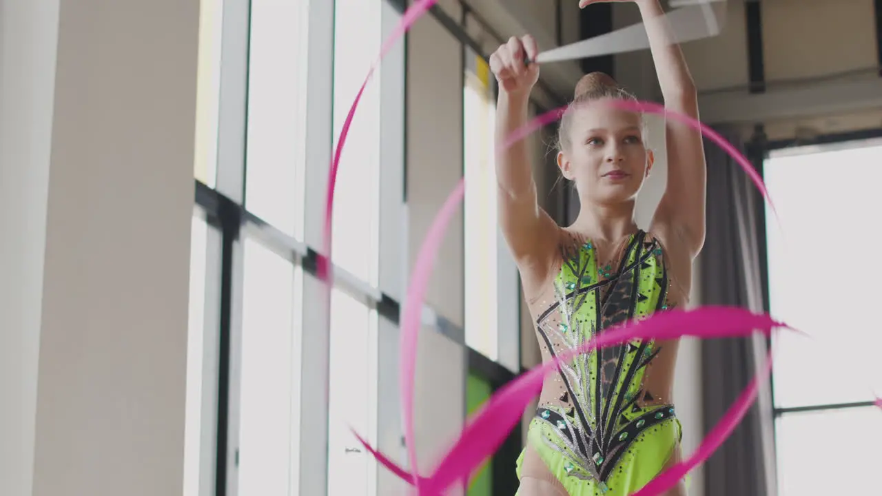 Smiling Young Girl In Leotard Practising Rhythmic Gymnastics With A Ribbon In A Studio