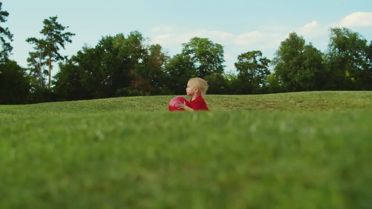 Boy walking in green field Cheerful child holding ball in hands outdoors