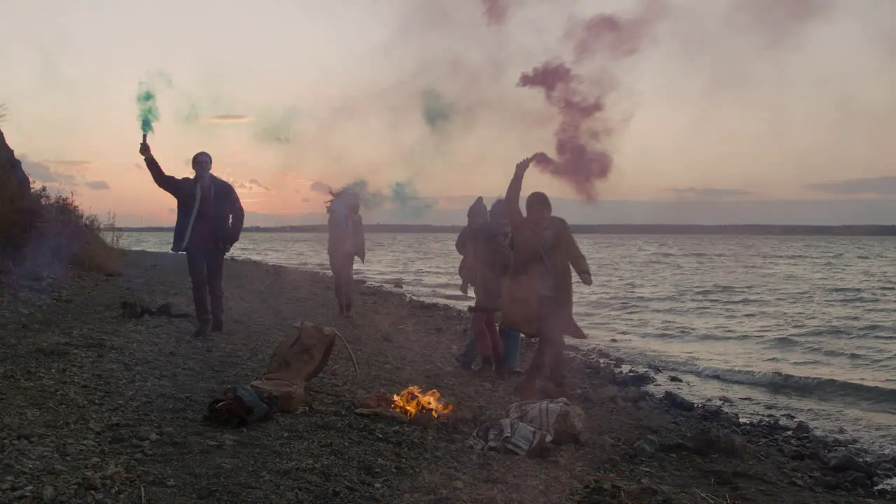 Group Of Teenage Friends Running Around A Bonfire Holding Colored Sparklers On The Seashore