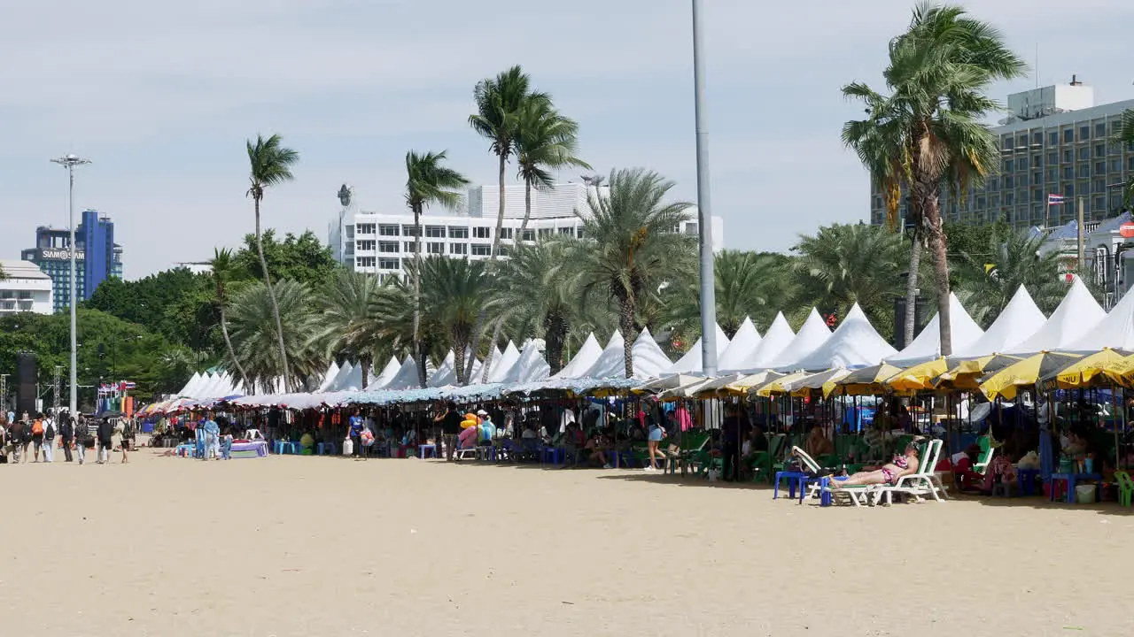 Busy beach with people under canopies and umbrellas while others walk around sunbathing during a windy day Pattaya Thailand