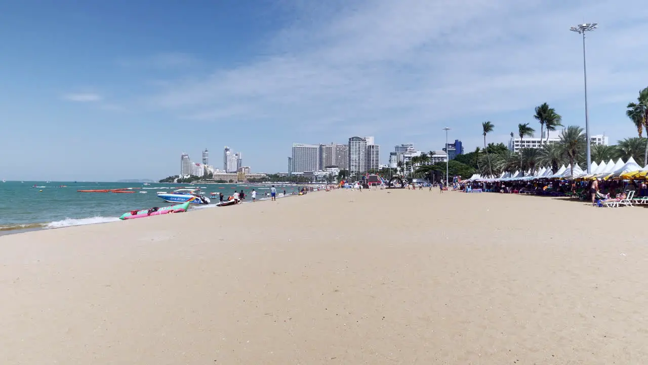 Tall buildings in the horizon hotels condominiums as people walkabout on the beach in Pattaya while other choose to stay under huge beach umbrellas and canopies Thailand