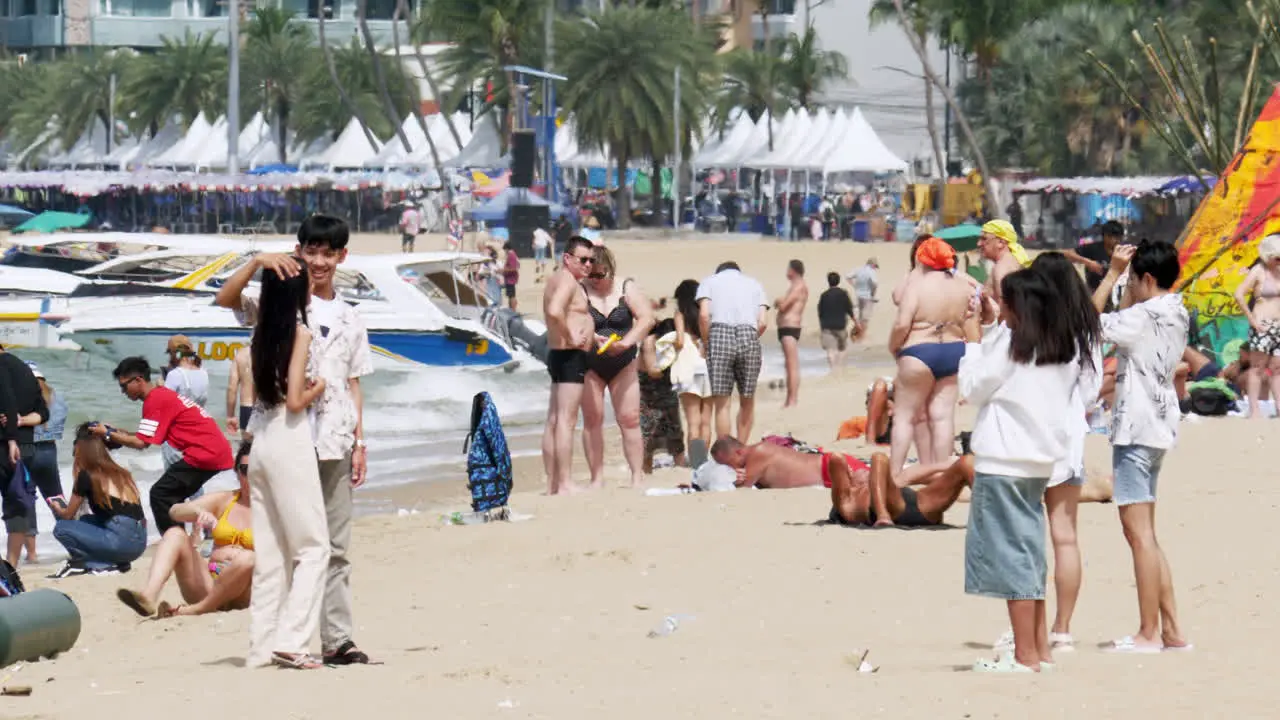 People enjoying the beach some sunbathing walking around taking pictures boats anchored a busy beach Pattaya Thailand