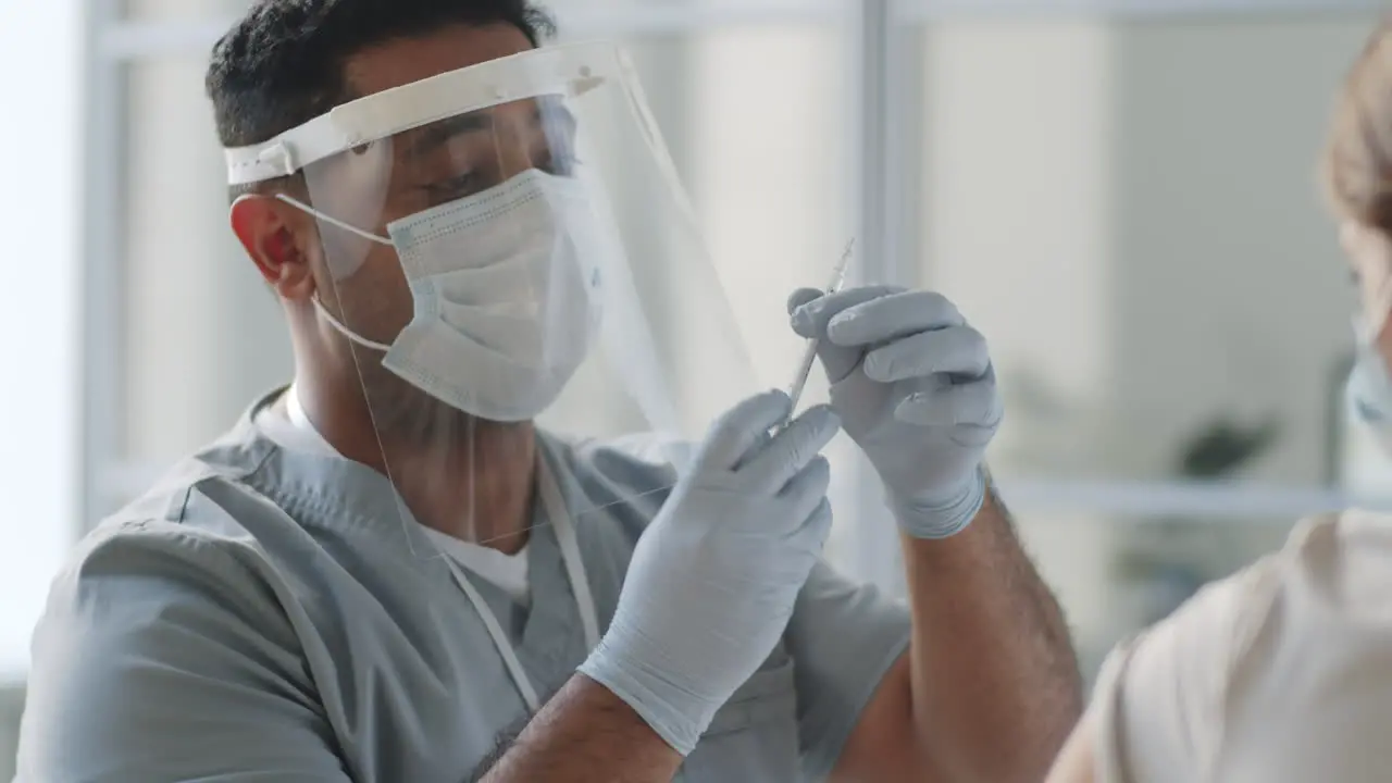 Doctor in Protective Uniform Vaccinating Female Patient