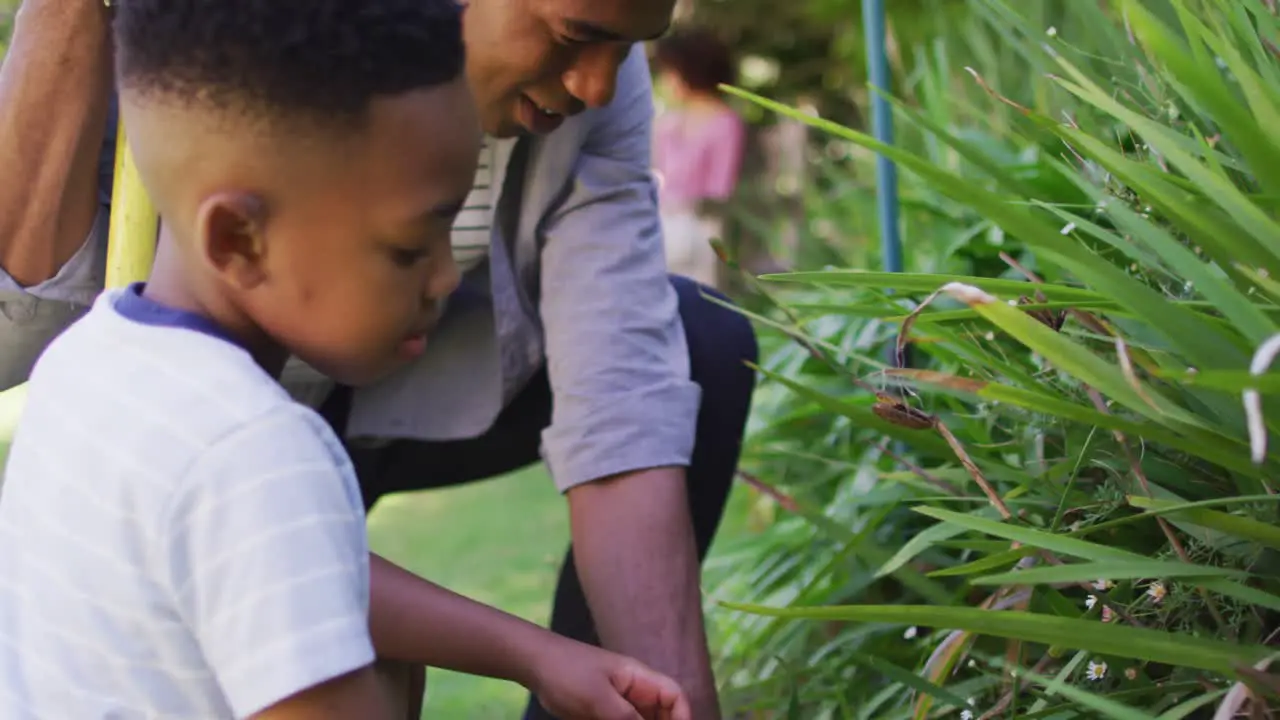 Happy african american father and son taking care of plants outdoors