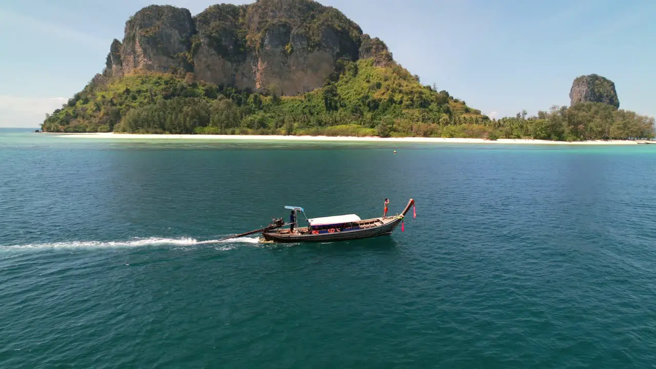 aerial drone parallel with a tourist at the front of a thai longtail boat motoring through the blue andaman sea on a sunny morning around the islands of Krabi Thailand with Ko Poda in the distance