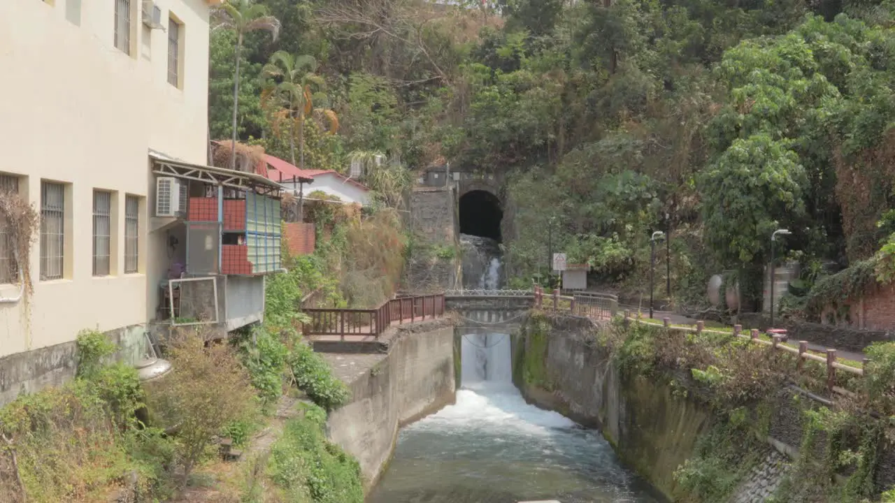 A waterfall spouting out water from the side of a hill and into a canal in a small village in southern Taiwan wide shot