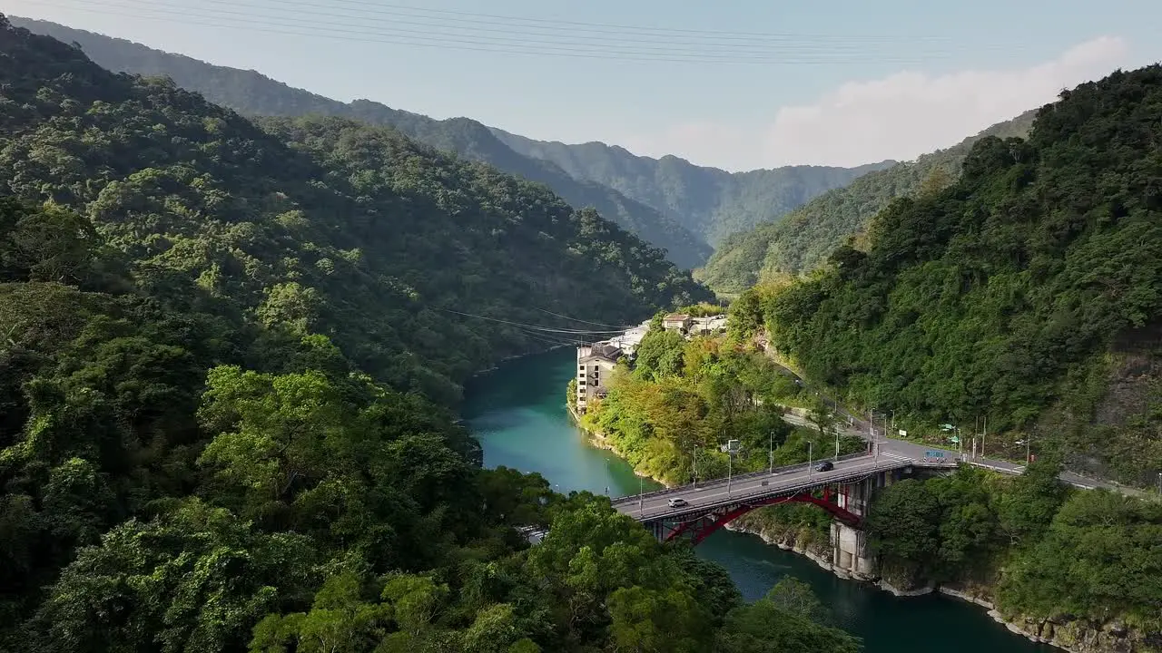 Aerial panning shot of cars on bridge Crossing river in green mountains of Wulai Taiwan