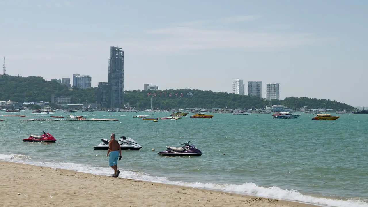 Foreign tourists taking a stroll at the sandy beachfront of Pattaya Beach against the background of the business hub of Chonburi province in Thailand