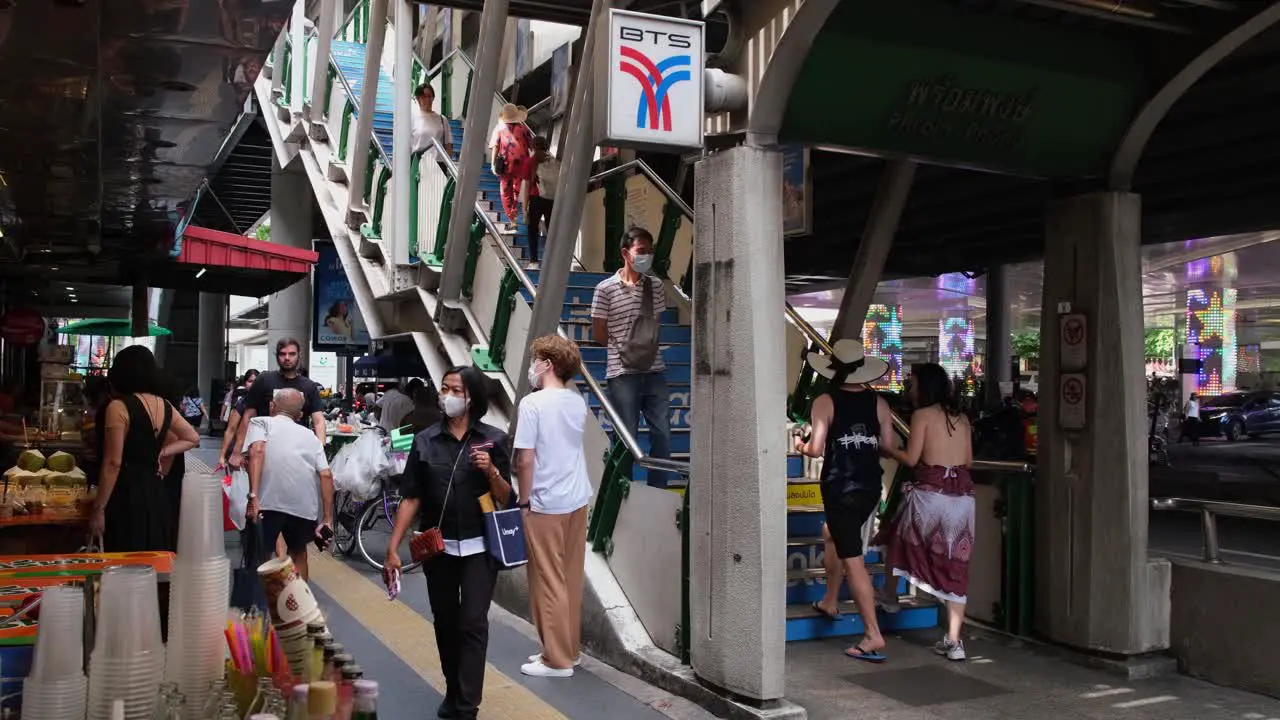 Commuters daily wage workers and tourists walking along the busy sidewalk of Sukhumvit road near Phrom Phong BTS train station with street food vendors on the sides in Bangkok Thailand