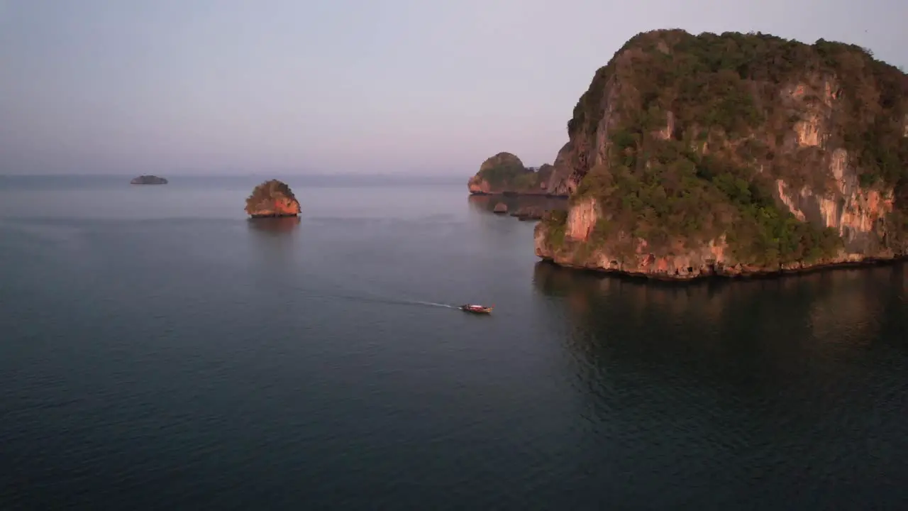 wide aerial circling a single thai longtail boat during sunrise near Railay Beach in Krabi Thailand around the beautiful limestone mountains of Krabi Thailand in the Andaman Sea