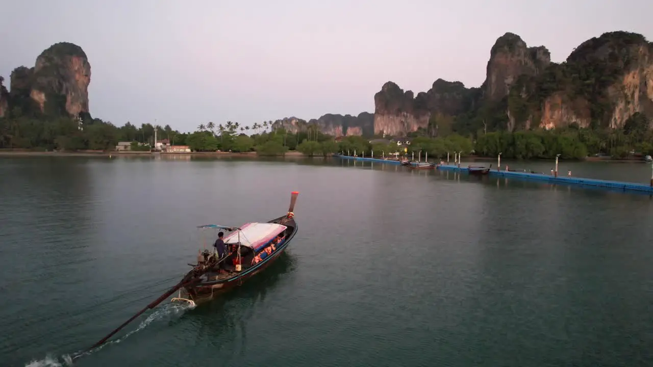 Thai longtail boat arriving at the docks in Railay Beach of Krabi Thailand during sunrise with large limestone rocks on the horizon