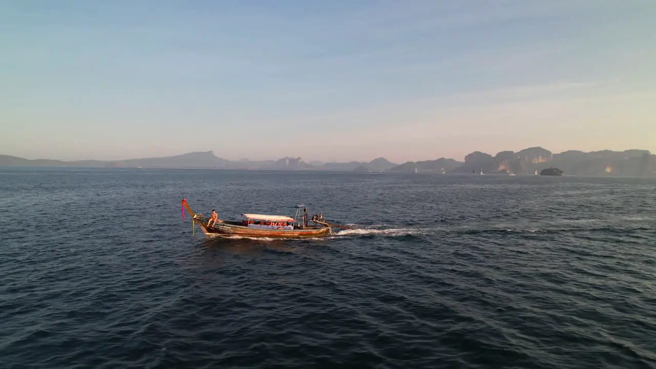 aerial drone tracking parallel with a thai longtail boat during a sunrise tour with a tourist on the front in Krabi Thailand