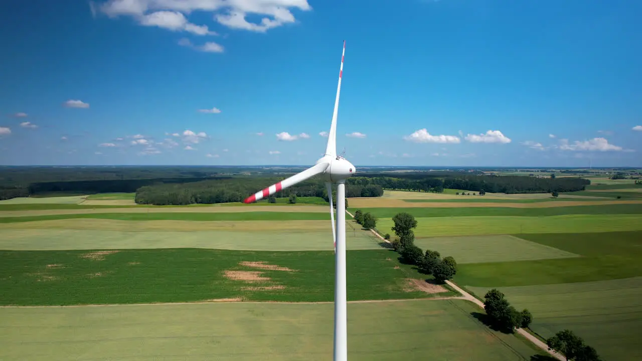 Spinning wind turbine in green farm lands with stunning blue sky aerial arc