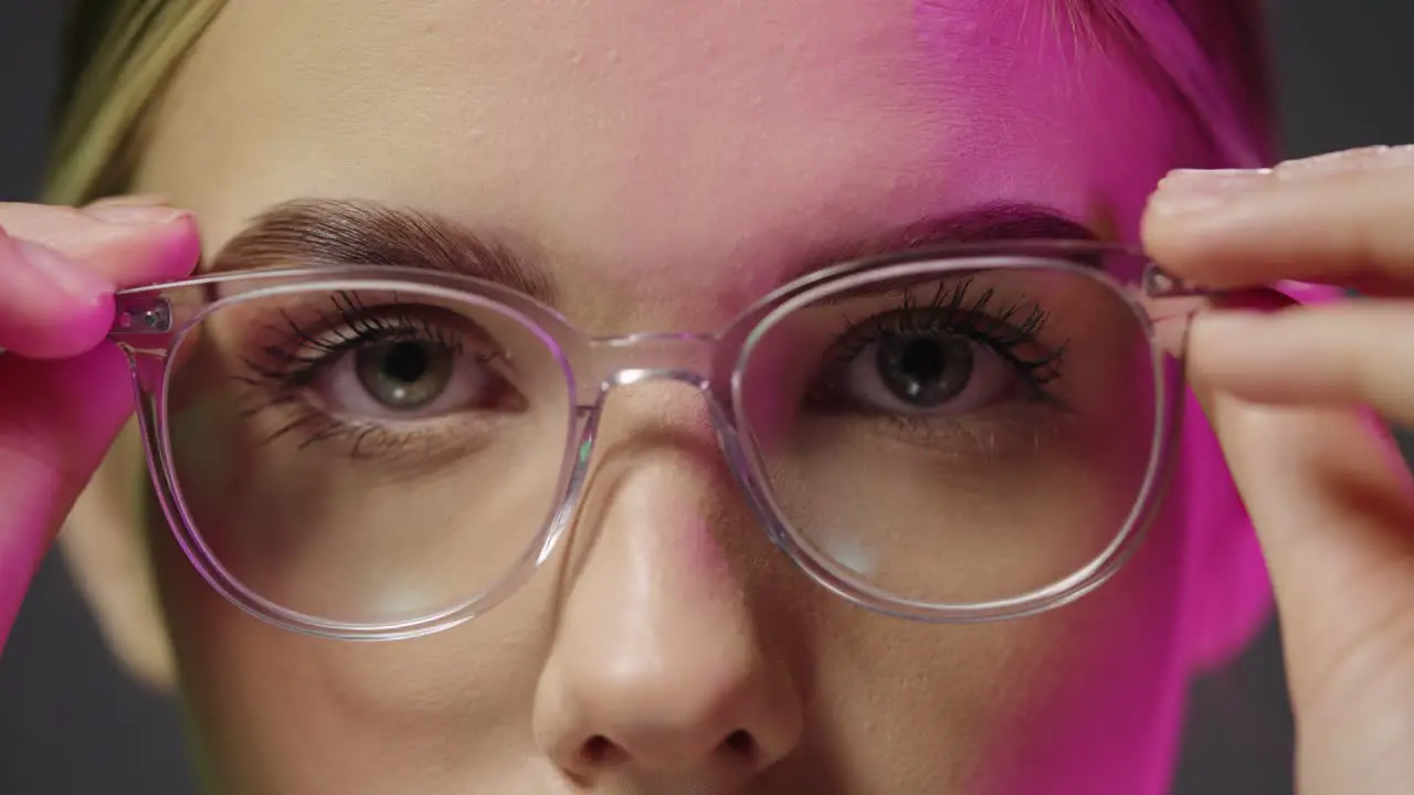 Close up of a young pretty beautiful woman while looking neutrally into the camera and taking on her glasses with purple light in her face in slow motion