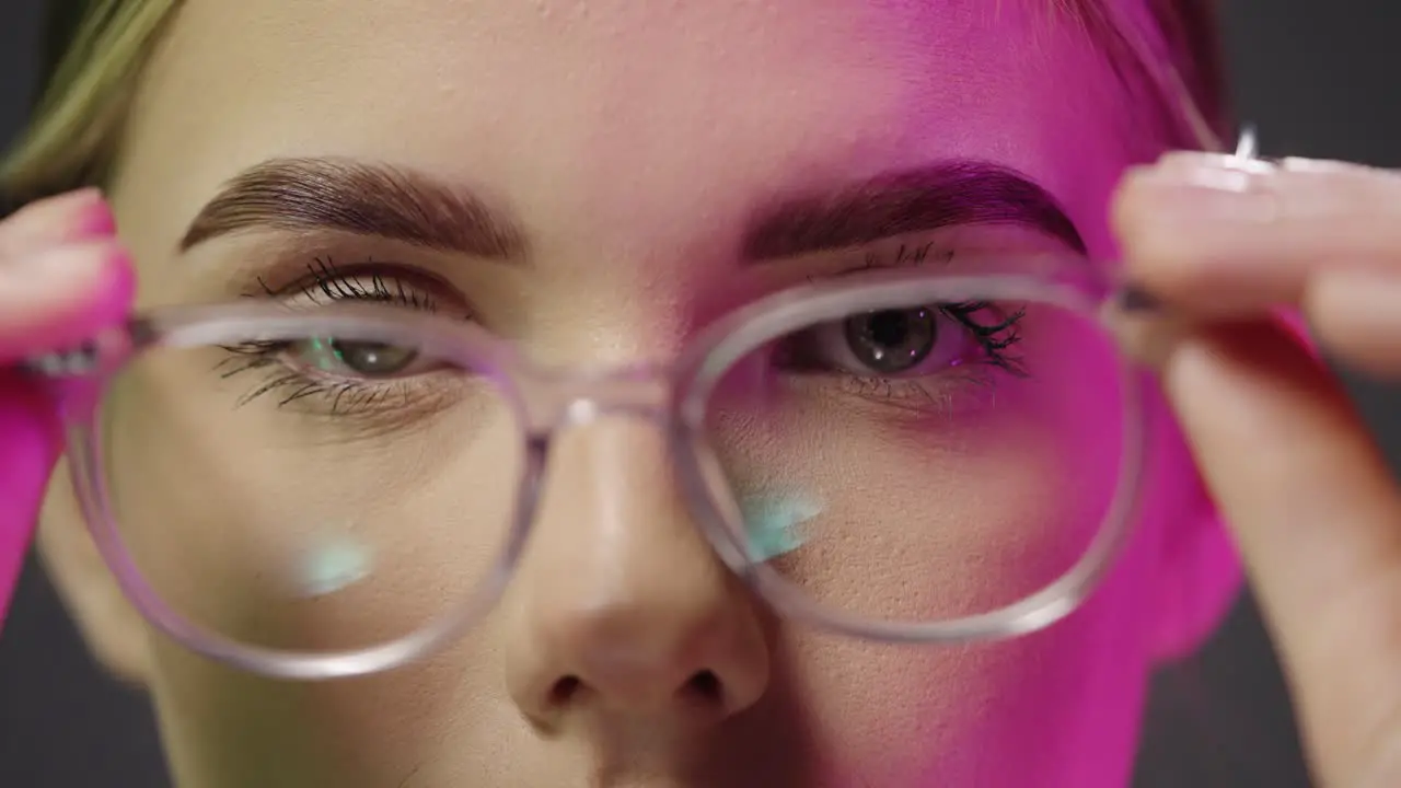 Close up of a young pretty woman wearing glasses while looking neutrally into the camera and taking off her glasses with purple light in her face in slow motion