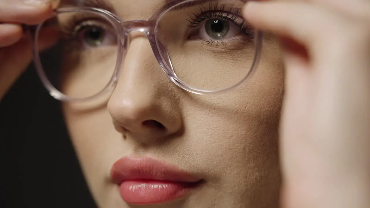 Close up tilt up of a young pretty woman putting on glasses as a visual aid for better vision to see more clearly with better eyesight in slow motion against black background