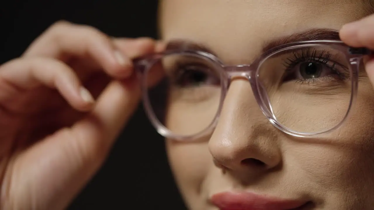 Close up of a young pretty woman putting on glasses as a visual aid for better vision to see more clearly with better eyesight in slow motion against black background