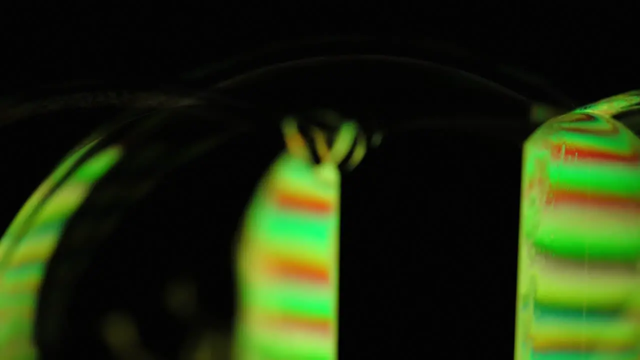 Dramatic close up of green and orange light refracting through and reflecting on spinning soap bubbles on black background macro