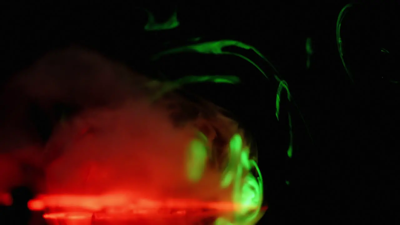 Slow tendrils of smoke pass through red and green lasers on black background abstract overlay