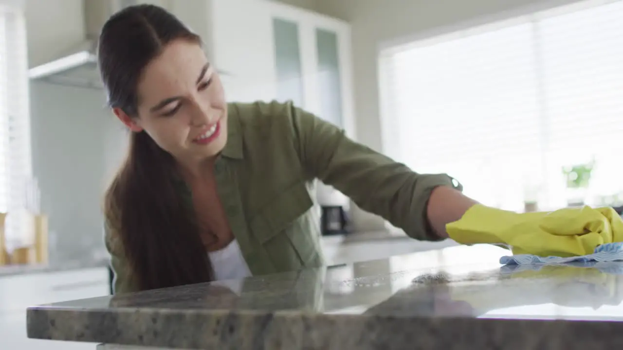 Caucasian woman wearing rubber gloves and cleaning table at home