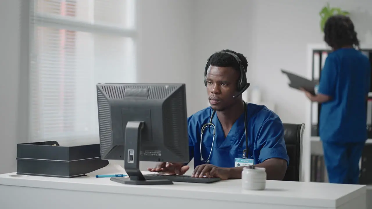 Afro-american male doctor or nurse with headset and computer working at hospital young professional therapist doctor consulting customer client using remote communication speaking on webcam