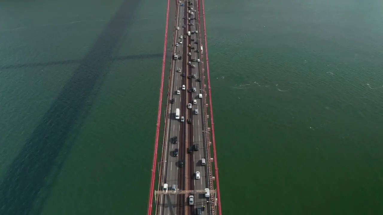 Aerial overhead view following a busy traffic driving across the sea on large red suspension Ponte 25 de Abril bridge in Lisbon Portugal