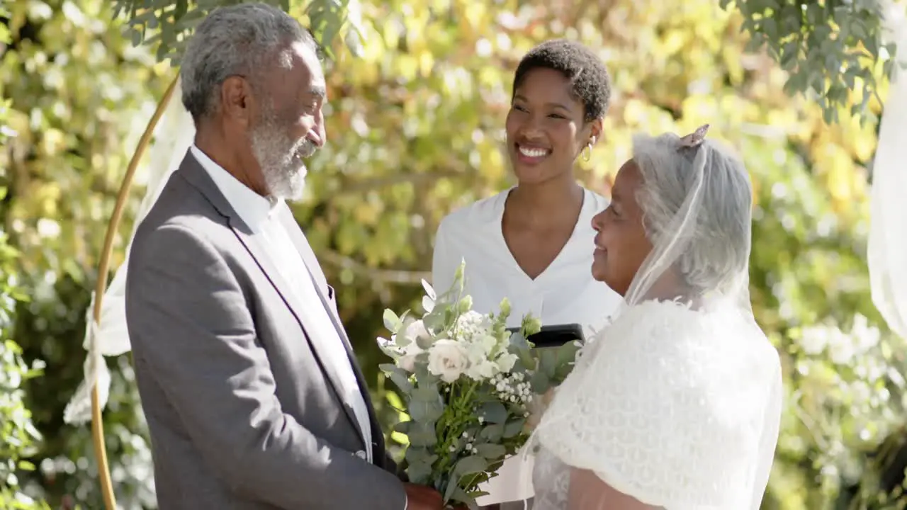 African american woman officiating wedding ceremony of senior biracial couple in garden slow motion