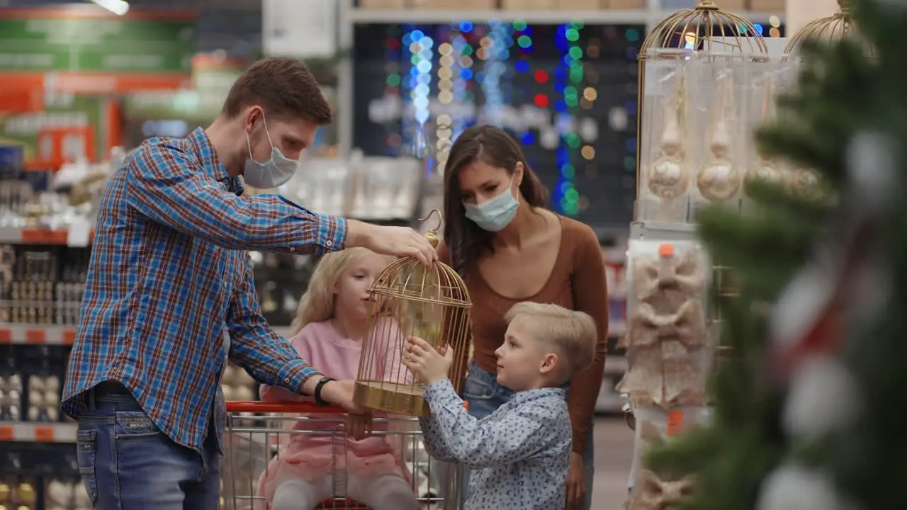 A happy family in medical masks in the store buys Christmas decorations and gifts in slow motion Four people father son daughter and mother